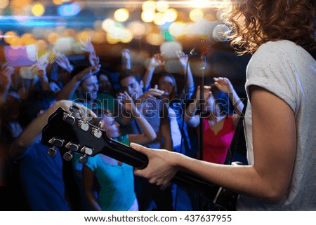 holidays, music, nightlife and people concept - close up of singer playing electric guitar and singing on stage over happy fans crowd waving hands at concert in night club