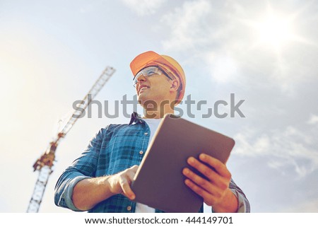 business, building, industry, technology and people concept - smiling builder in hardhat with tablet pc computer over group of builders at construction site