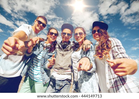 summer holidays and teenage concept - group of smiling teenagers in sunglasses hanging outside pointing finger at you