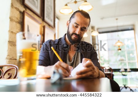 people, inspiration, freelance and leisure concept - man with beer writing to notebook at bar or pub