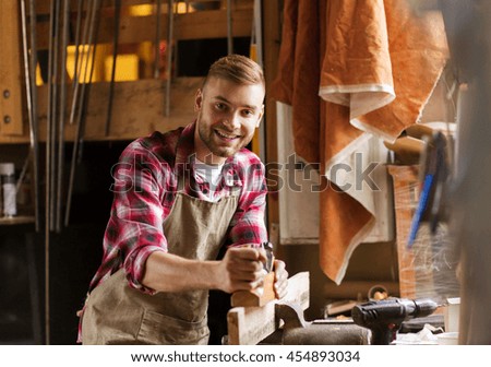 profession, people, carpentry, woodwork and people concept - happy carpenter with jointer planing wood plank at workshop