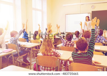 education, elementary school, learning and people concept - group of school kids with teacher sitting in classroom and raising hands