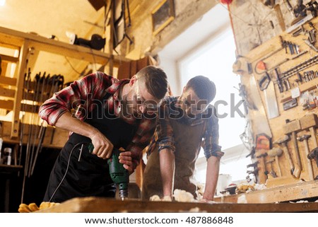 profession, carpentry, woodwork and people concept - two carpenters with electric drill drilling wood plank at workshop