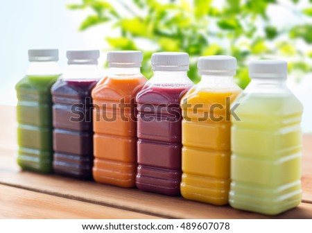 healthy eating, drinks, dieting and packaging concept - plastic bottles with different fruit or vegetable juices on wooden table over green natural background