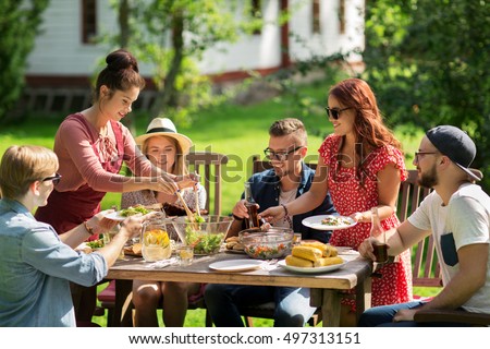 leisure, holidays, eating, people and food concept - happy friends having dinner and sharing salad at summer garden party