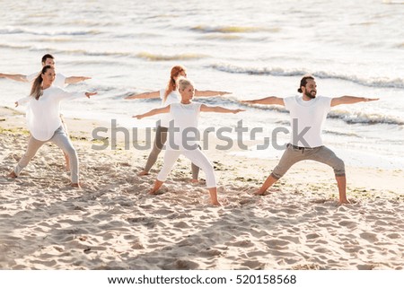 fitness, sport and healthy lifestyle concept - group of people making yoga in warrior pose on beach