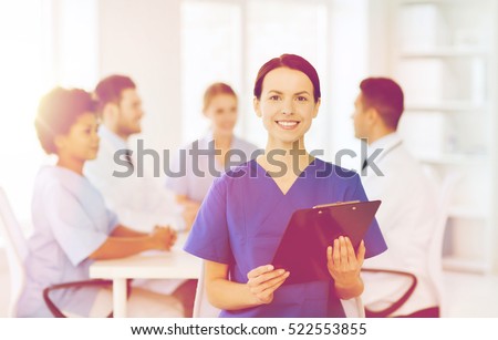 clinic, profession, people and medicine concept - happy female doctor or nurse with clipboard over group of medics meeting at hospital