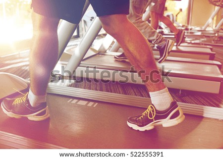 sport, fitness, lifestyle, technology and people concept - close up of men legs walking on treadmills in gym