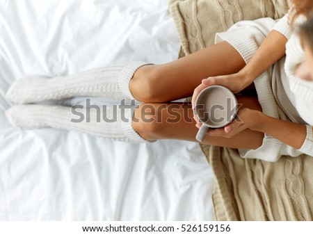 morning, coziness, winter and people concept - close up of young woman with cup of coffee or cacao in bed at home
