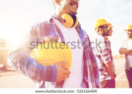 building, protective gear and people concept - close up of builder holding yellow hardhat or helmet at construction site
