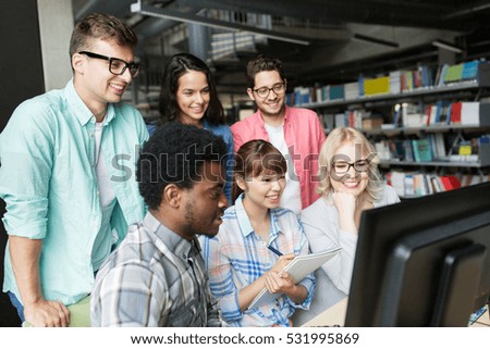 people, education, technology and school concept - group of happy smiling international students with computers at library in university