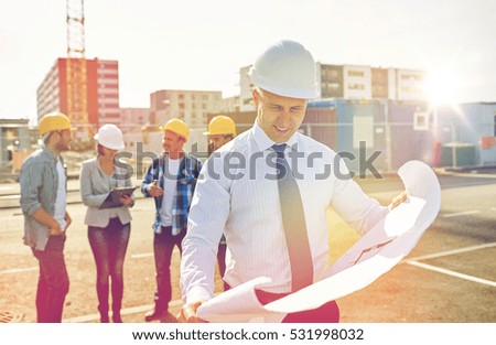 construction, architecture, business, teamwork and people concept - male architect with blueprint over group of builders on construction site