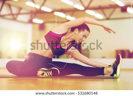 fitness, sport, training, gym and lifestyle concept - stretching young woman with earphones in the gym