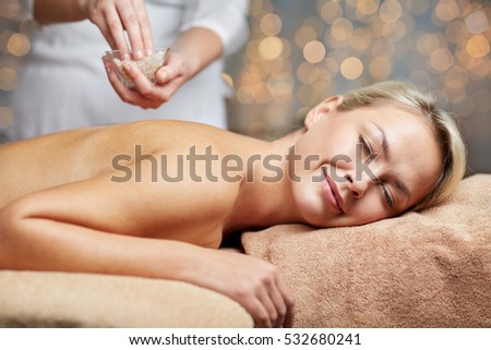people, beauty, spa, massage and relaxation concept - close up of beautiful young woman lying with closed eyes and therapist holding salt bowl in spa