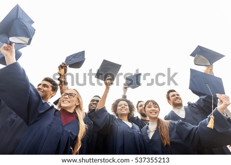 education, graduation and people concept - group of happy international students in bachelor gowns waving mortar boards or hats