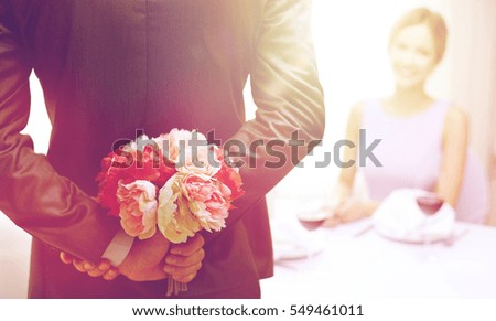 restaurant, people, celebration and holiday concept - close up of man hiding flowers behind from woman at restaurant