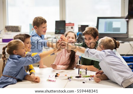 education, children, technology, science and people concept - group of happy kids building robots and making high five gesture at robotics school
