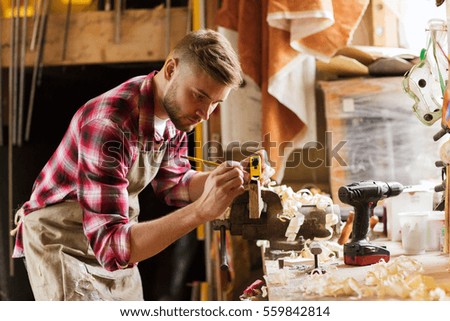 profession, carpentry, woodwork and people concept - carpenter with ruler measuring wood plank at workshop