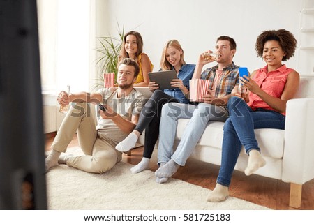 friendship, people, technology and entertainment concept - happy friends with tablet pc computer and smartphone eating popcorn, drinking beer or cider and watching tv at home