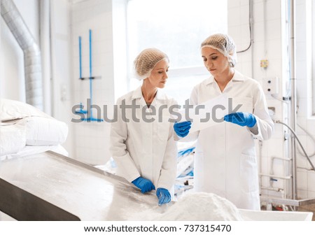 manufacture, industry, food production and people concept - women technologists with paper and powdered milk at ice cream factory shop