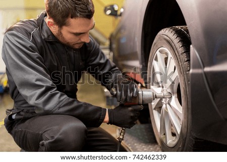 car service, repair, maintenance and people concept - auto mechanic man with electric screwdriver changing tire at workshop