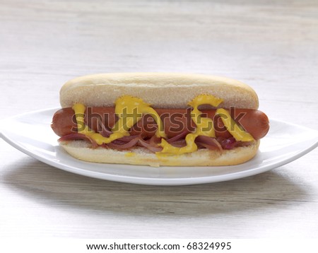 a sausage in a small bread with mustard and onions in a plate