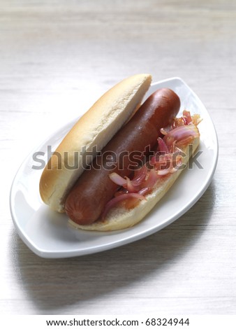 a sausage in a small bread with onions in a plate