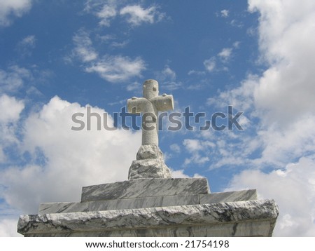Stone cross atop granite cemetery tomb with blue sky & clouds in background