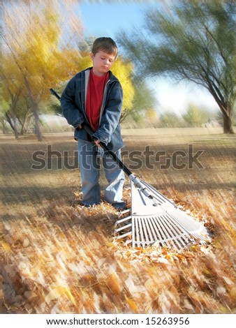 Unhappy boy raking autumn leaves in yard