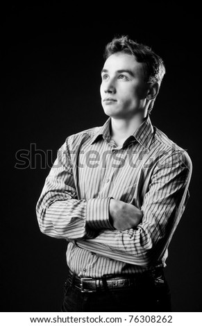 Black and white portrait of a young guy in the studio. Dressed in a shirt and his hands folded on his chest.