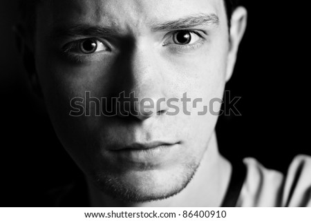 Portrait of angry guy looks into the camera. Glare in his eyes. Black and white.