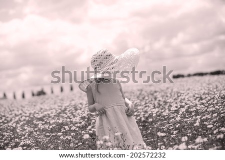 Young child standing in a flower field, wearing a large sun hat, black and white image