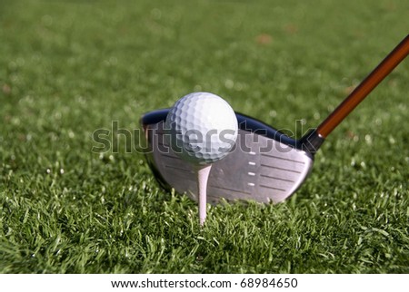 Golf ball on tee about to be hit by a driver.