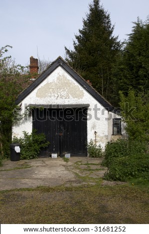 An old detached garage with a grass driveway