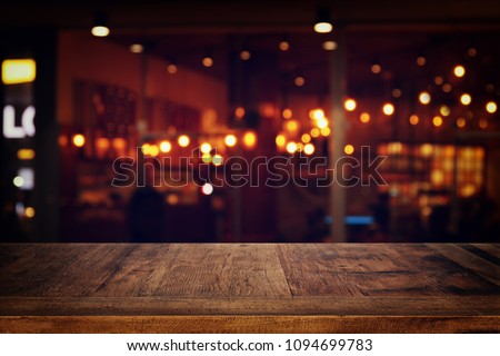 Image of wooden table in front of abstract blurred restaurant lights background