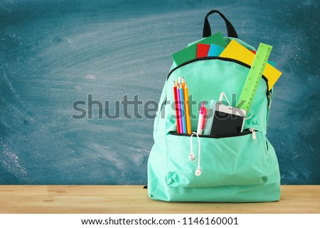 school bag with stationery and notebooks in front of blackboard. Back to school concept