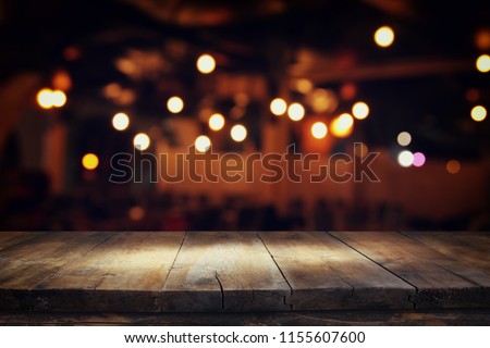 Image of wooden table in front of abstract blurred restaurant lights background