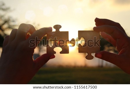 Concept image of a woman hands holding two pieces of a puzzle in front of the sun. Sunset time with lens flare. creativity and connectivity idea