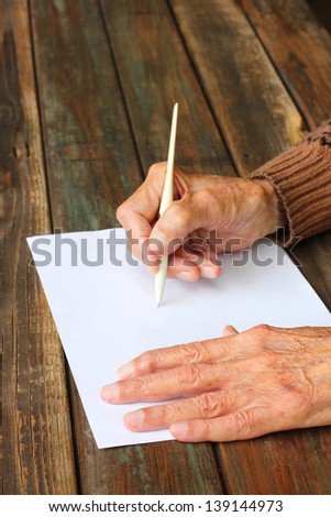 close up of elderly male hands on wooden table . writing on blank paper
