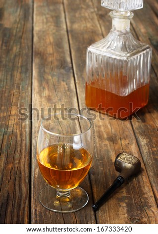 Whiskey drink, bottle and vintage smoking pipe on wood table.