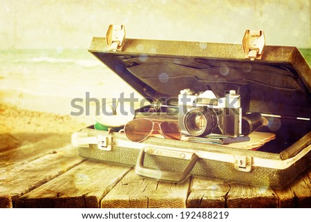 open case with old camera sunglasses and clock in front of seascape. filtered image.