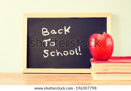 blackboard with the phrase back to school, apple and stack of books. filtered image