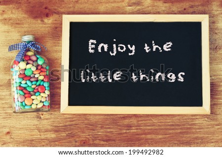bottle filled with candies and blackboard with the phrase enjoy the little things.