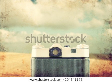 back view of vintage camera in front of field landscape. filtered and textured image.