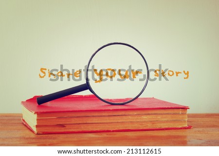 magnifying glass , old book with the phrase share your story. filtered image.