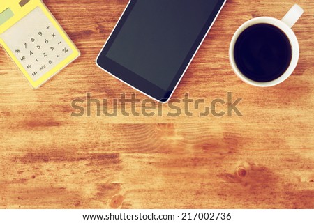 top view of tablet, coffee cup and calculator over wooden textured table background. image is toned.