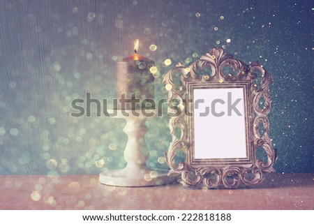 low key image of vintage antique classical frame and Burning candle on wooden table and glitter lights background . filtered image