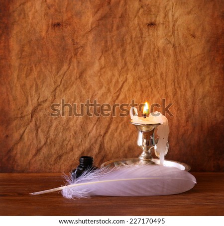 low key image of white Feather, inkwell and burning candle on a wooden table