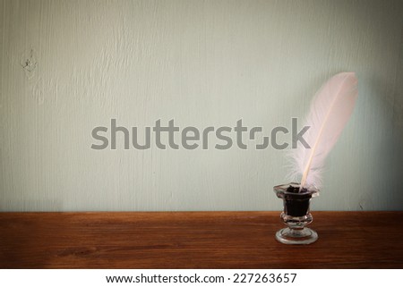 low key image of white Feather and inkwell on old wooden table