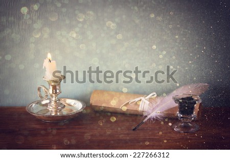 low key image of white Feather, inkwell, scroll and candle and  glitter lights background on old wooden table